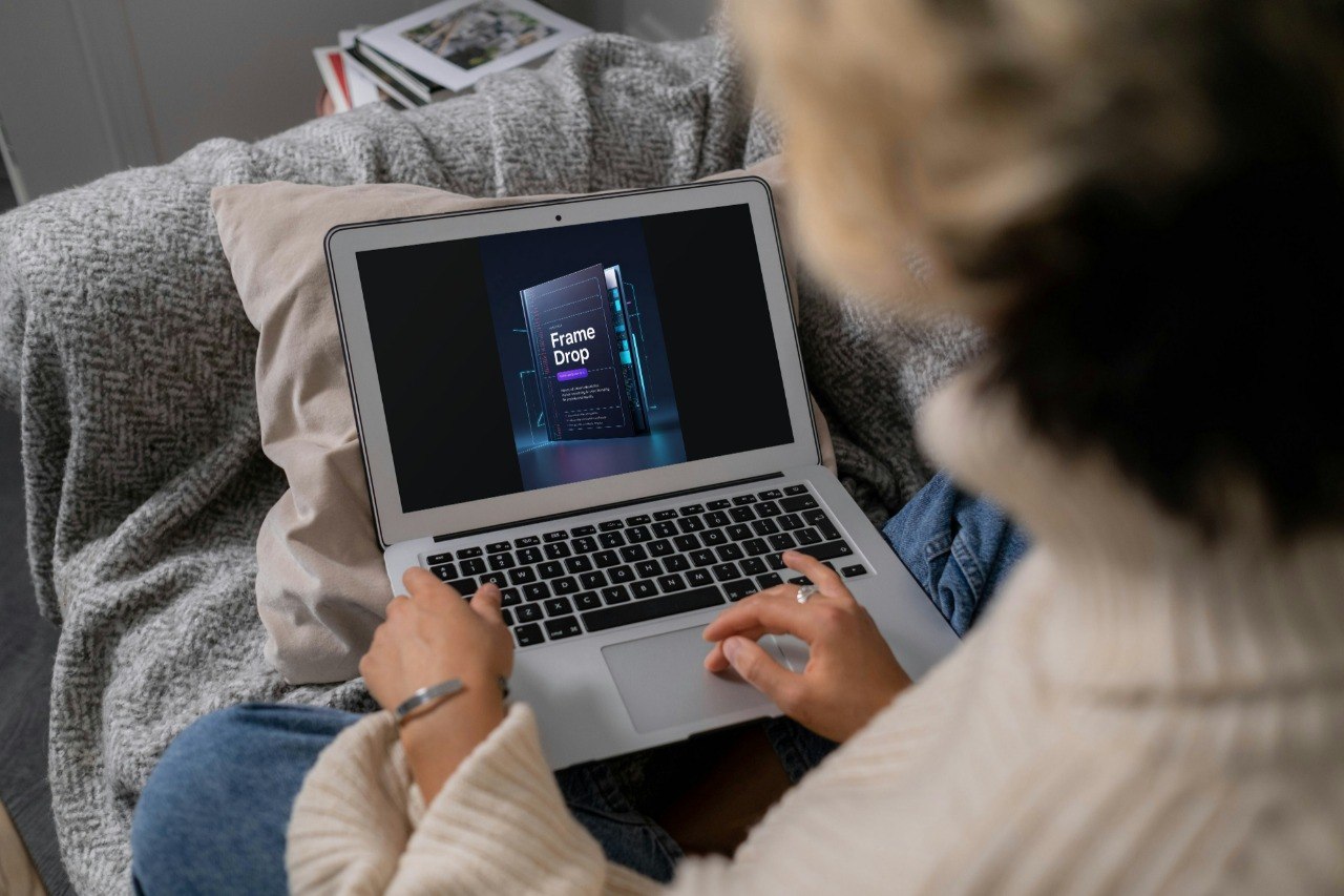 A person sitting on a couch uses a silver laptop showing a course or video titled 'Frame Drop'.